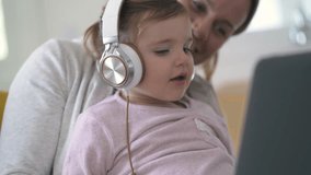 Adorable young girl with headphones looking at computer with mother