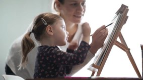Mother showing adorable young daughter how to draw on easel at home