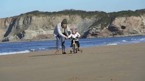 Slow motion of mother running next to young daughter cycling on beach