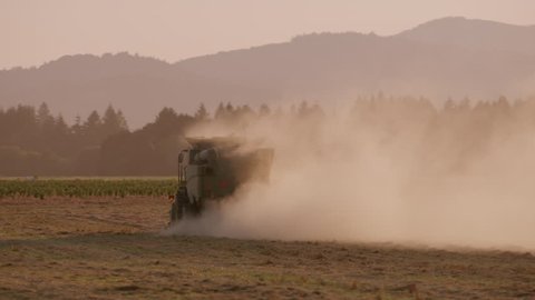 Combine working in dusty field at sunset, Oregon. Circa 2018