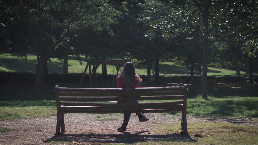 lonely thoughtful woman sitting alone on the bench in the park- back view