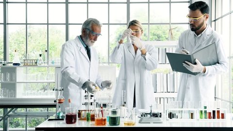 Group of chemists working in a lab. Young white male and female chemists with senior caucasian chemist working together in lab, taking notes. Science concept.