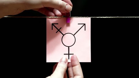 On the white sheet is image of transgender symbol. The sheet is attached manually with a clothespin on the rope.