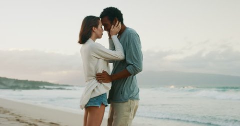 Happy young couple embracing and kissing on tropical beach at sunset
