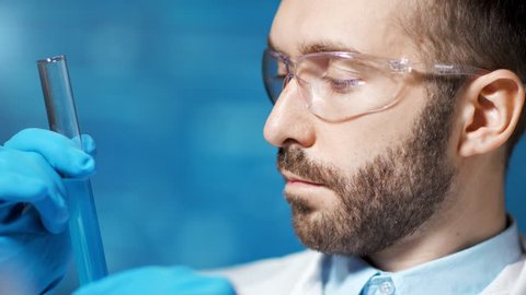 Undistracted male chemist holding beaker with blue substance making experience in lab close-up
