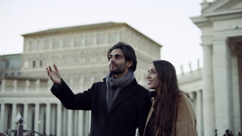 Happy Italian couple walking around St Peter's Square looking at the architecture and talking together in Rome, with soft natural lighting. Wide shot on 4k RED camera.