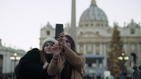 Two excited Italian friends looking out at St Peter's Basilica in St Peter's Square in the Vatican taking silly face pictures together with soft natural lighting. Medium shot on 4k RED camera. Video Stok
