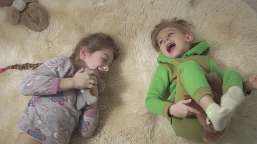 Two adorable children rolling on the fluffy carpet. Brother and sister have a fun. Happy kids weekend.