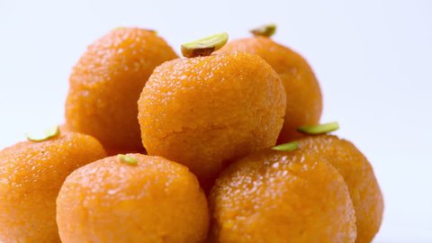Motichoor ladoos (indian sweet) in orange color revolving on white plate against white background