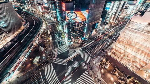 Tokyo, Japan - Jan 13, 2019: 4K UHD Aerial view time-lapse of Ginza road intersection at night, with crowded people walking on zebra crossing and car traffic light trails