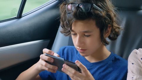 teen boy uses phone while traveling in car