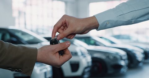 Close up of dealer giving key to new owner in auto show or salon. Slow motion shot in 8K. Concept of car dealerships, used cars, car sale and rent, auto deal