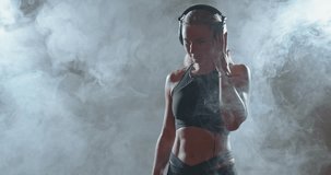 Beautiful sporty girl in headphones while listening to the music in the smoke. Studio video