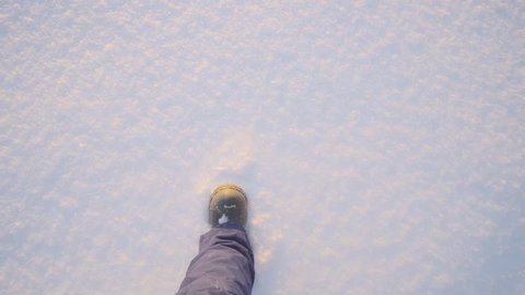 POV shot little cute child legs wearing warm shoes walking on clean smooth snow surface of white snowdrift top view. Confident baby kid enjoying walking outdoor in amazing winter park in cold day