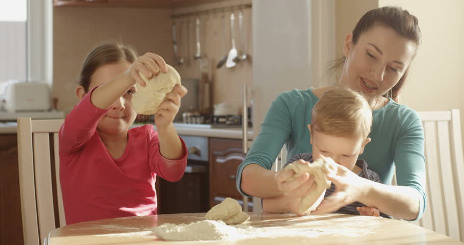 Family Portrait of Mother with Her Children Having Fun Kneading Dough and Stretching and Preparing Cooking Together a Cake Sitting at the Kitchen Table on a Sunny Day Royalty-Free Stock Footage #1022663332