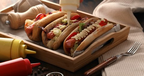 Hot dogs with a sausage on a fresh rolls garnished with mustard and ketchup. Men hand hand pouring hotdog with sauce