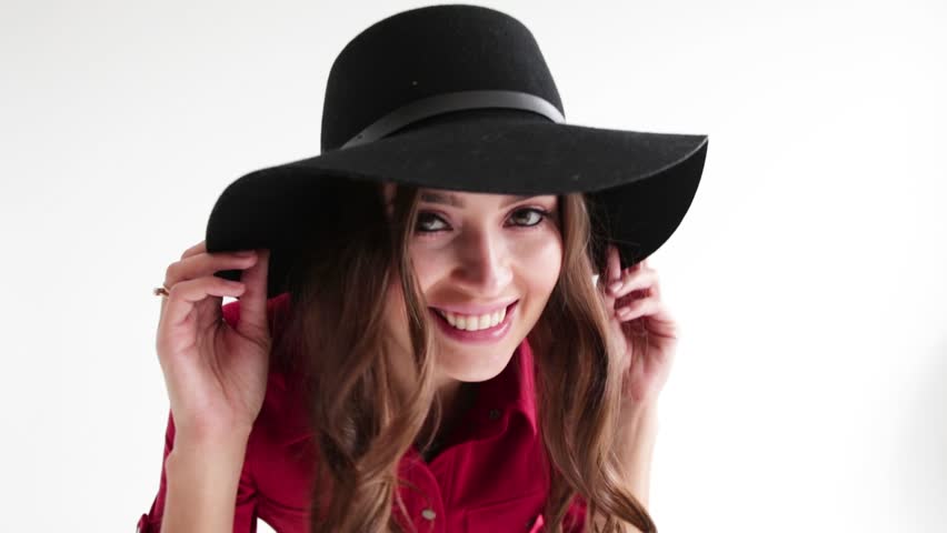 The girl tries on a black hat and dances. The girl with blond hair smiles and laughs in a black hat