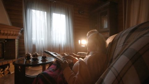 An elderly couple considers a family photo album wrapped in a blanket sitting by a cozy fireplace. Golden wedding, happy marriage, grow old together Stock Video