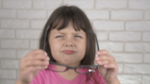 A child with poor eyes wears glasses. Little girl puts on glasses for sight. No focus.