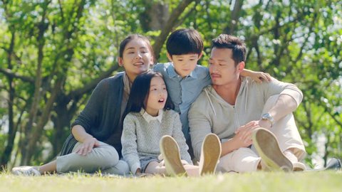 asian family with two children sitting on grass outdoors in a park talking chatting