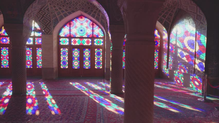 Shiraz, Iran - 31 October, 2018: Panning motion of colorful stained glass windows inside the Nasir al-Mulk Mosque. Morning sunlight reflected on columns, the wall and the floor of prayer hall. Royalty-Free Stock Footage #1022675320