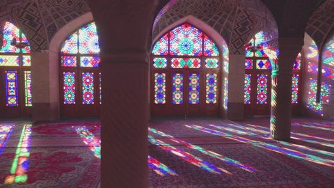Shiraz, Iran - 31 October, 2018: Panning motion of colorful stained glass windows inside the Nasir al-Mulk Mosque. Morning sunlight reflected on columns, the wall and the floor of prayer hall.