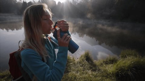 Hiker woman drinking on mountain lake trail from water bottle
