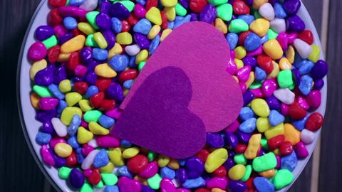 Two multicolored decorative hearts on a background of bright multi-colored pebbles. The concept of Valentine's Day and love.