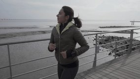Smiling brunette hindu woman running on pier at seaside. Cheerful sportswoman training outdoor. Concept of sport