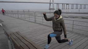 Confident young hindu woman training on seaside. Focused brunette sportswoman stretching legs on wooden pier. Concept of sport