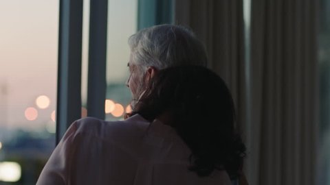 happy couple hugging at home looking out window at sunset enjoying successful retirement lifestyle on vacation sharing romantic connection