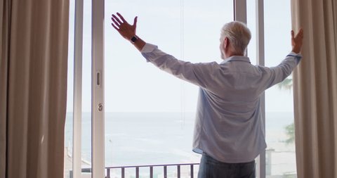 happy old man dancing enjoying beautiful view of ocean in hotel room celebrating successful retirement vacation