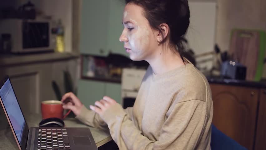 Young girl caring for skin. Mask on the face. She uses a laptop. HD