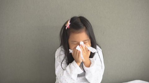 Asian child or kid girl sick with sneezing on nose and cold cough on tissue paper because weak or virus and bacteria from dust weather and kindergarten and pre school for medical background gray space