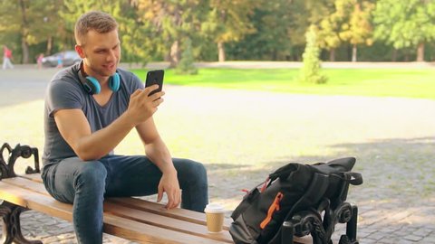 handsome young man sitting on the bench using smartphone. caucasian guy scrolling touch screen happy smiling
