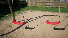 Children’s swings swaying in the wind in a children’s playground
Slow motion video of two empty red children’s swings swaying in the wind in a children’s playground