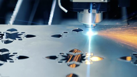 Industrial laser machine cuts metal parts from sheets. Sparks fly to the side.