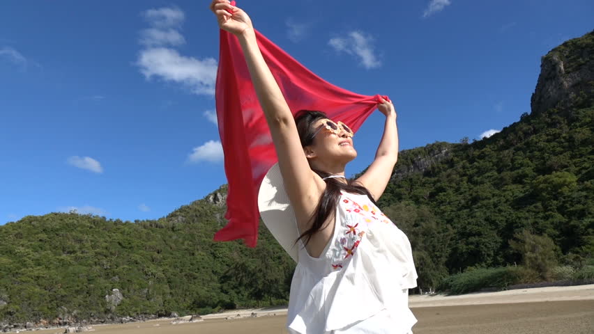 Happy woman with silk fabric standing on beautiful beach, feel free with sunny sea view