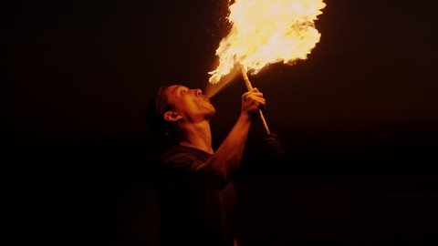 Cool fire show artist juggles his torch breathes fire in dark air, performing amazing stunts - slow motion