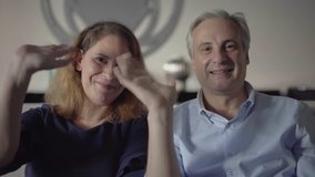 Couple of middle aged parents talking to adult children. Front view of man and woman waving hands, saying Hello, nodding and speaking at camera. Video chat concept