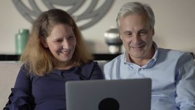 Couple of parents talking to adult children. Middle aged man and woman sitting on couch and using laptop for video call. Distance communication concept