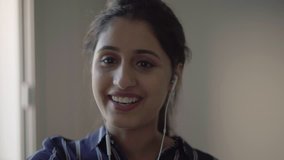 Laughing girl with earphones using smartphone for video call. Young woman talking to mobile phone screen, telling funny story or gossip. Video talk concept