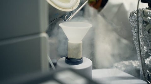 Slow motion pouring liquid nitrogen through a funnel into container in laboratory