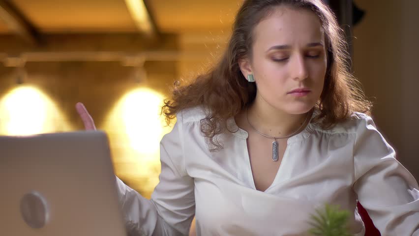 Portrait of young curly-haired woman joyfully dancing and singing in her seat in office.