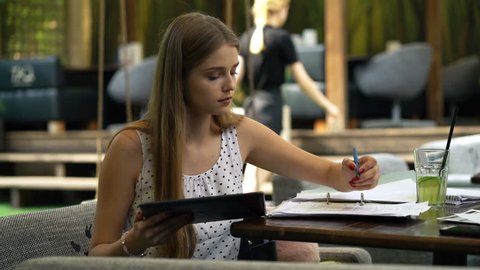 Young girl student doing homework with tablet computer in cafe