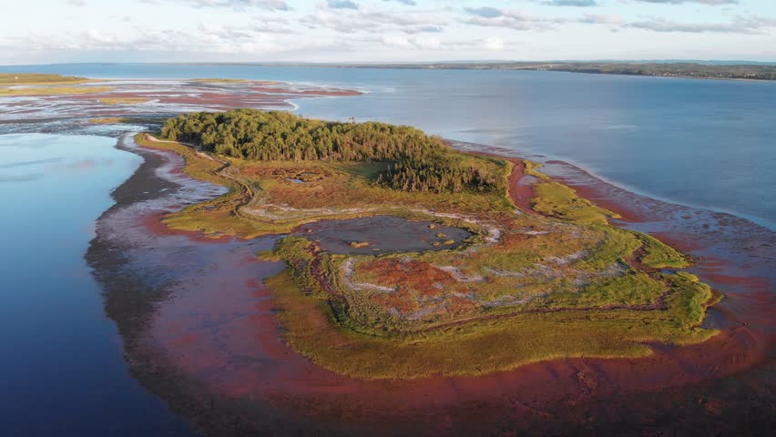 Aerial, drone shot, above a island, at shallow, blue sea, on the coast of Nova Scotia island, on a sunny morning, in Canada
