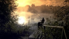 A fisherman at dawn catches fish in a beautiful place on a lake or river. Morning fog sunny day. Relaxing beautiful video in 4 to resolution