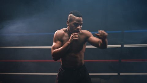 A muscular African American boxer shadow boxes towards the camera in a hazy boxing ring