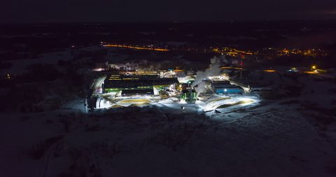 4K aerial hyperlapse of a busy wood factory at winter night. Tractors feeding timber to the production building.