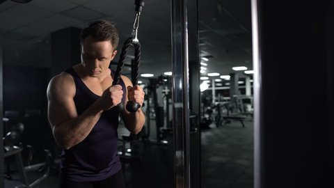 Athletic man training arm muscles, performing triceps cable pushdown exercise